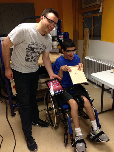 Two makers in front of a CNC machine holding up a wooden ipad holder